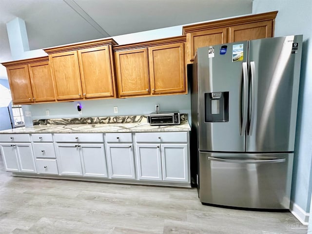 kitchen with light stone counters, light hardwood / wood-style floors, white cabinetry, and stainless steel refrigerator with ice dispenser