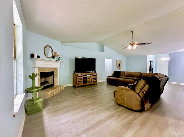 living room with lofted ceiling, ceiling fan, a tiled fireplace, and wood-type flooring