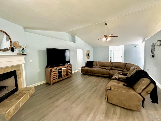 living room featuring lofted ceiling, ceiling fan, a tiled fireplace, and hardwood / wood-style floors