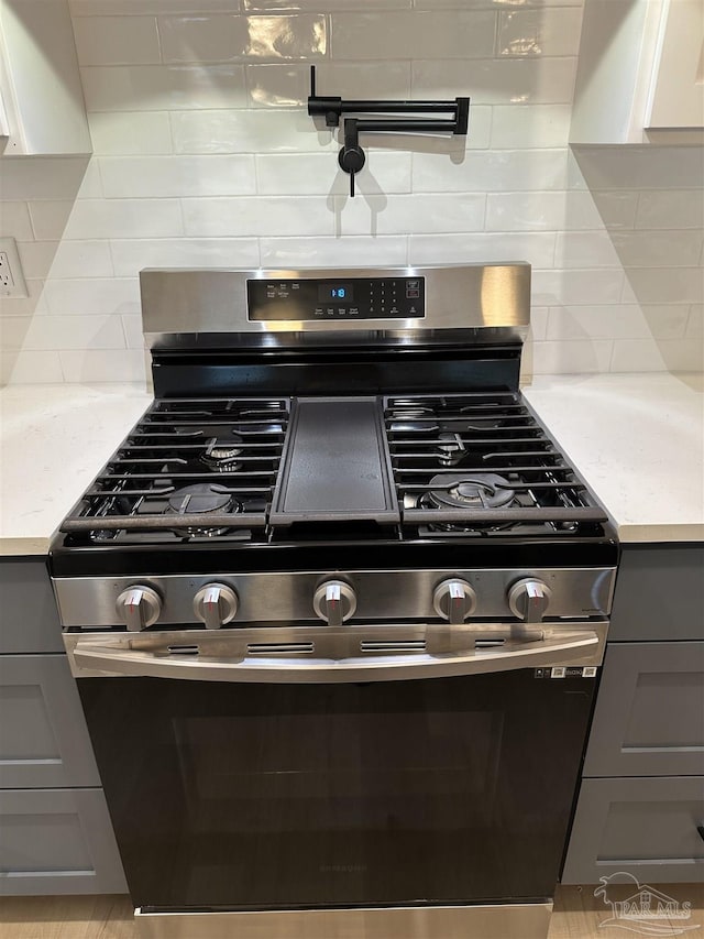 room details with light stone countertops, stainless steel range with gas cooktop, white cabinets, and backsplash