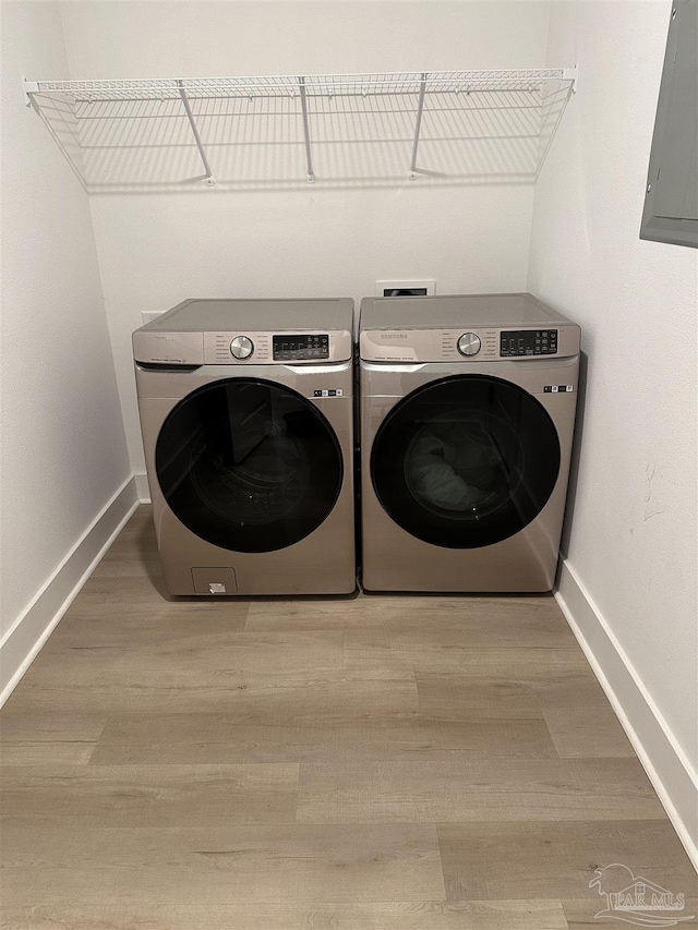 clothes washing area with laundry area, separate washer and dryer, wood finished floors, baseboards, and electric panel