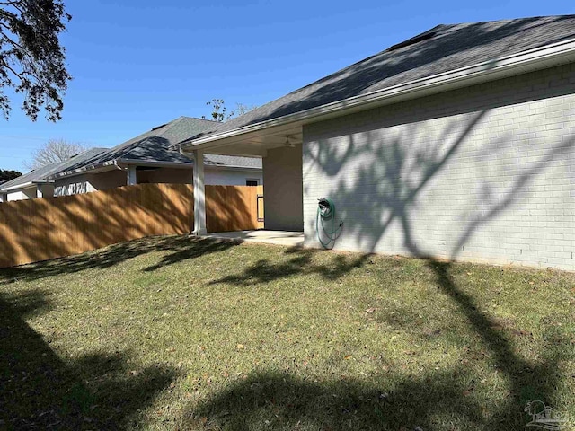 view of home's exterior featuring a yard, brick siding, a shingled roof, and fence