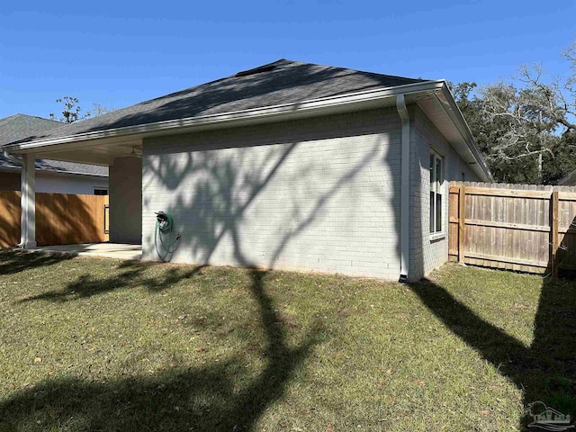 view of side of home with a yard, brick siding, roof with shingles, and fence