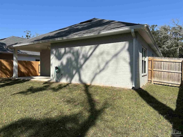 view of side of home with fence, a lawn, and brick siding