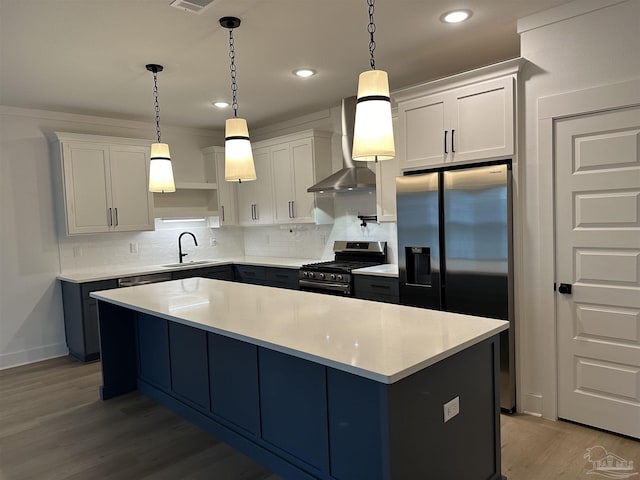 kitchen featuring stainless steel appliances, a sink, hanging light fixtures, light countertops, and wall chimney exhaust hood