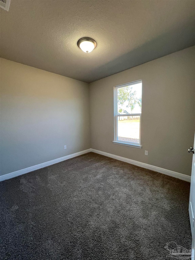 empty room with dark colored carpet and a textured ceiling