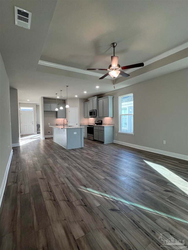 kitchen with gray cabinets, a raised ceiling, an island with sink, sink, and stainless steel appliances