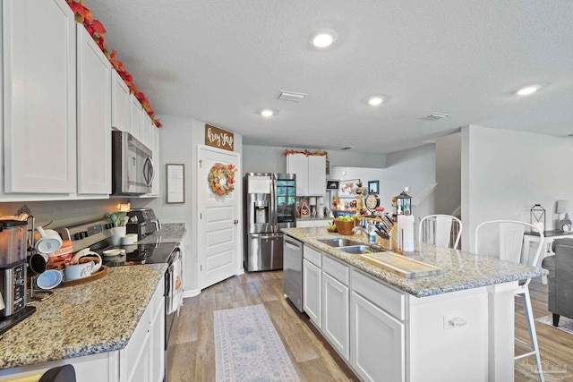 kitchen featuring light wood-type flooring, a kitchen island with sink, stainless steel appliances, and white cabinets