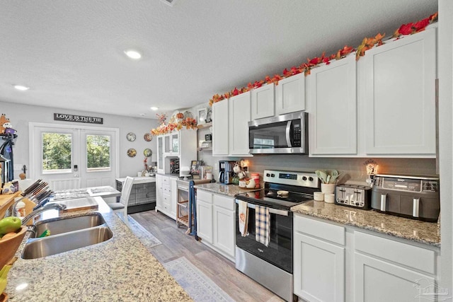 kitchen with sink, appliances with stainless steel finishes, light wood-type flooring, and white cabinetry