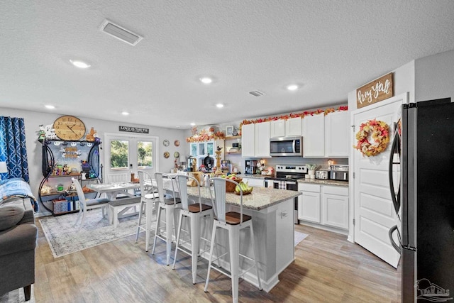 kitchen featuring stainless steel appliances, a center island with sink, a kitchen bar, white cabinetry, and light hardwood / wood-style floors