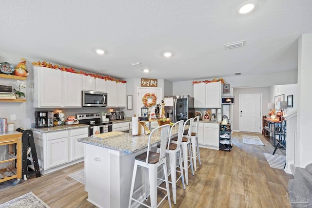 kitchen featuring a kitchen island with sink, appliances with stainless steel finishes, light hardwood / wood-style flooring, and white cabinets