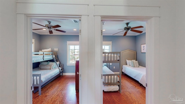 bedroom with baseboards, crown molding, visible vents, ceiling fan, and wood finished floors