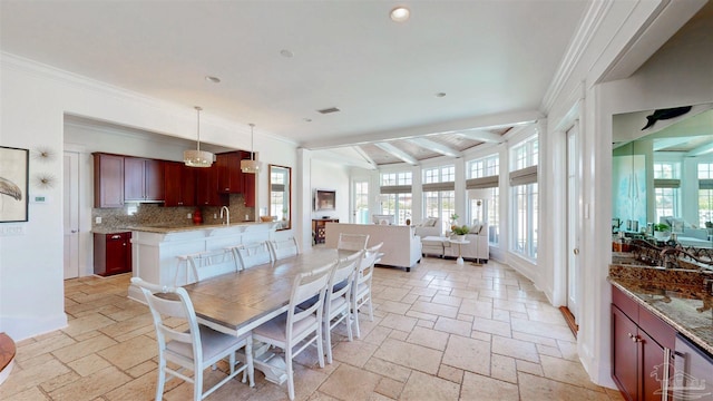 dining space with plenty of natural light, stone tile floors, ornamental molding, and beam ceiling