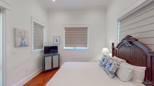bedroom with multiple windows, baseboards, crown molding, and wood finished floors