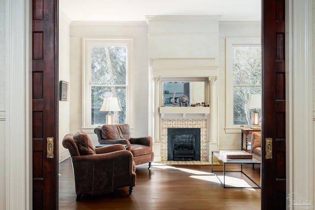 living area with wood-type flooring, ornamental molding, and a tiled fireplace