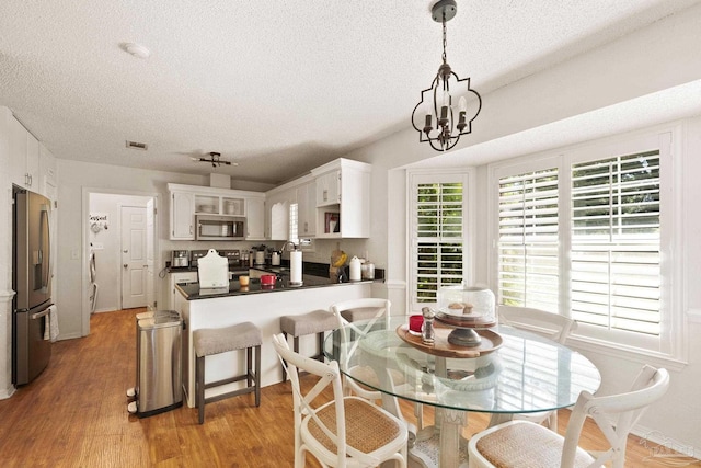 dining room with a notable chandelier, a textured ceiling, visible vents, and light wood-style floors