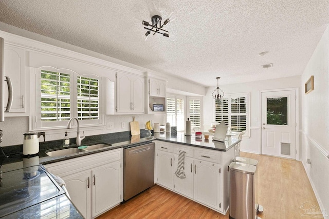 kitchen featuring dark countertops, a peninsula, stainless steel dishwasher, white cabinetry, and a sink