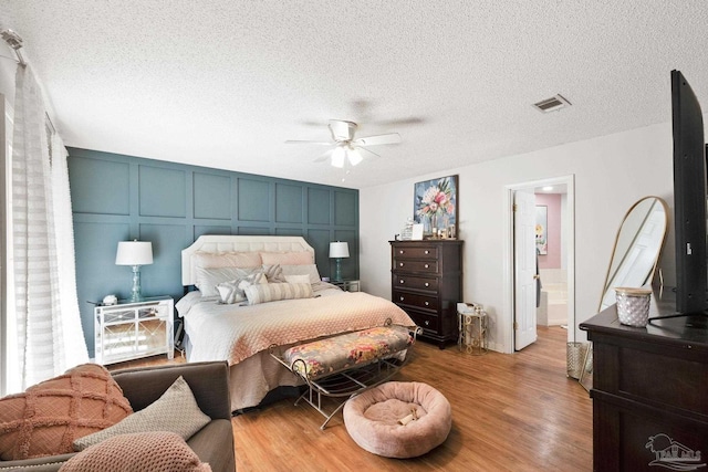 bedroom featuring visible vents, ceiling fan, wood finished floors, a textured ceiling, and a decorative wall