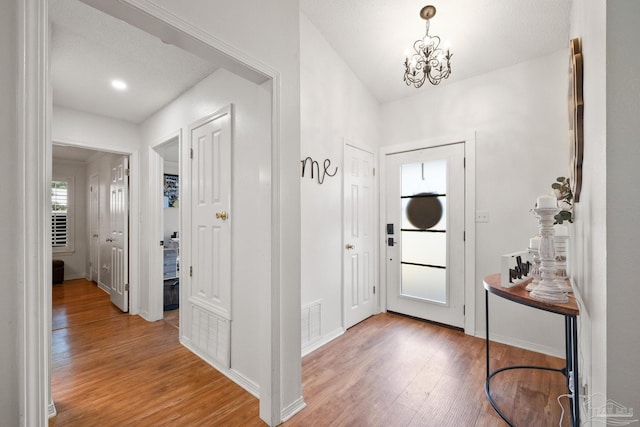 foyer entrance with visible vents, a notable chandelier, baseboards, and wood finished floors