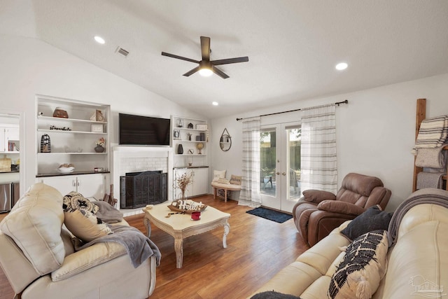 living room featuring visible vents, lofted ceiling, wood finished floors, french doors, and a brick fireplace