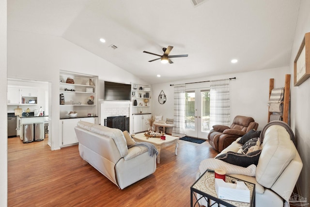 living area with ceiling fan, vaulted ceiling, french doors, light wood-type flooring, and a brick fireplace