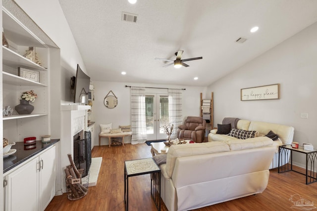 living room featuring visible vents, a fireplace with flush hearth, dark wood-type flooring, vaulted ceiling, and french doors