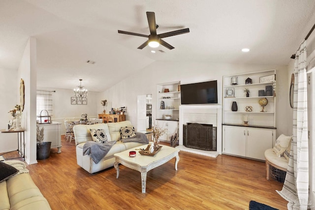 living area featuring lofted ceiling, light wood-style floors, a brick fireplace, and ceiling fan with notable chandelier