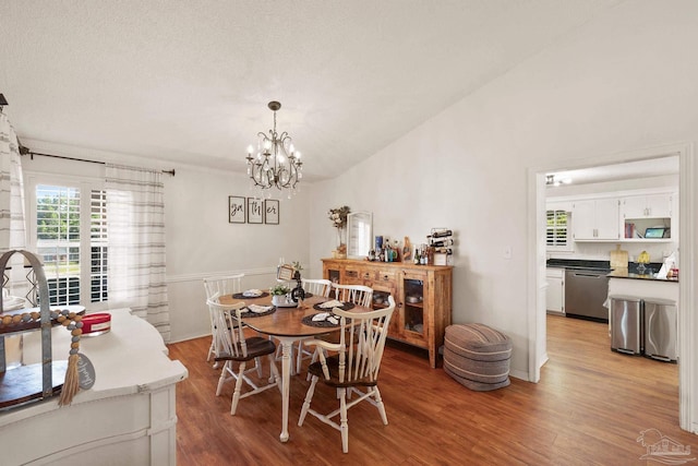 dining space with vaulted ceiling, a textured ceiling, wood finished floors, and an inviting chandelier