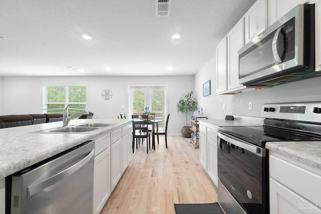 kitchen with light wood-type flooring, white cabinetry, sink, and appliances with stainless steel finishes