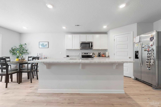 kitchen with light hardwood / wood-style flooring, stainless steel appliances, white cabinetry, and an island with sink