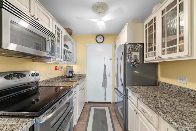 kitchen with ceiling fan, appliances with stainless steel finishes, light stone countertops, dark tile patterned floors, and sink