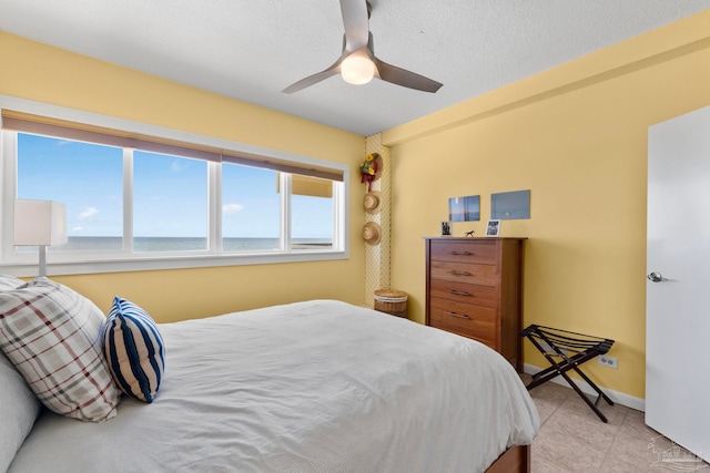 bedroom with a textured ceiling, a water view, and ceiling fan