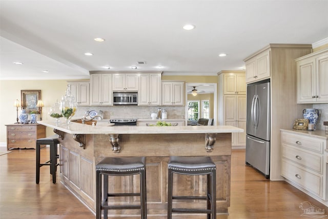 kitchen featuring a kitchen bar, stainless steel appliances, decorative backsplash, cream cabinetry, and light wood-style flooring
