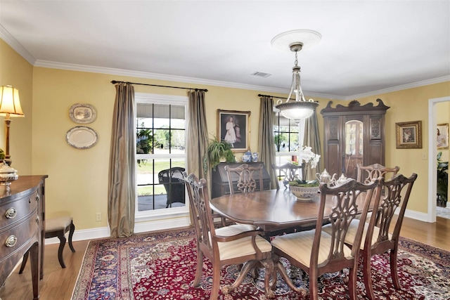 dining space featuring baseboards, visible vents, wood finished floors, and ornamental molding