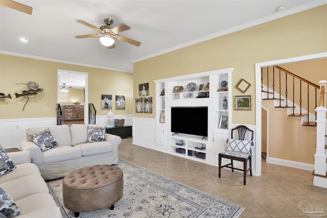 tiled living area featuring a wainscoted wall, ceiling fan, stairs, and ornamental molding