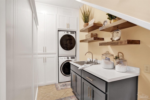 washroom featuring light tile patterned flooring, cabinet space, stacked washing maching and dryer, and a sink
