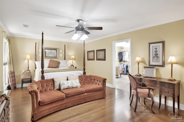 bedroom with a walk in closet, crown molding, baseboards, and wood finished floors
