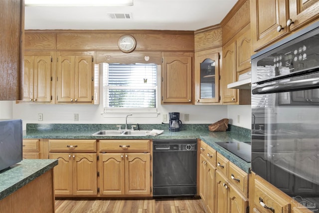 kitchen featuring visible vents, light wood finished floors, dark countertops, a sink, and black appliances