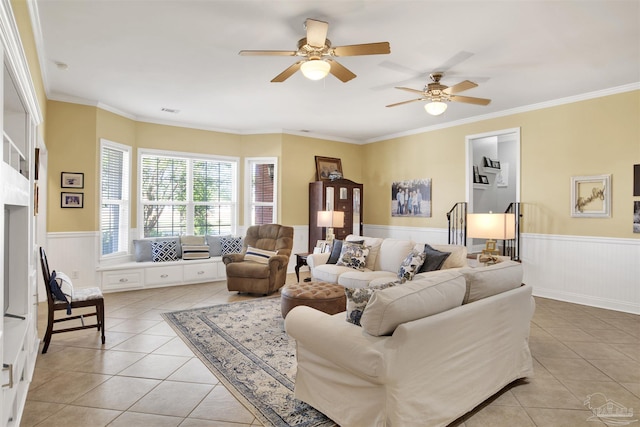 living room featuring light tile patterned flooring, ornamental molding, ceiling fan, and wainscoting
