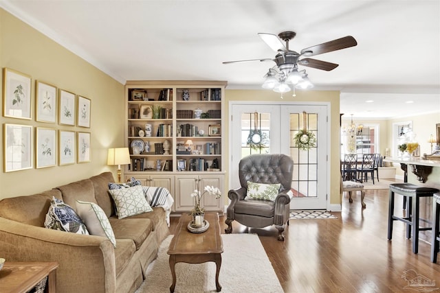 living area featuring wood finished floors, ornamental molding, ceiling fan with notable chandelier, and a wealth of natural light