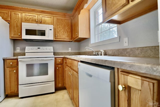 kitchen featuring brown cabinetry, white appliances, light countertops, and a sink