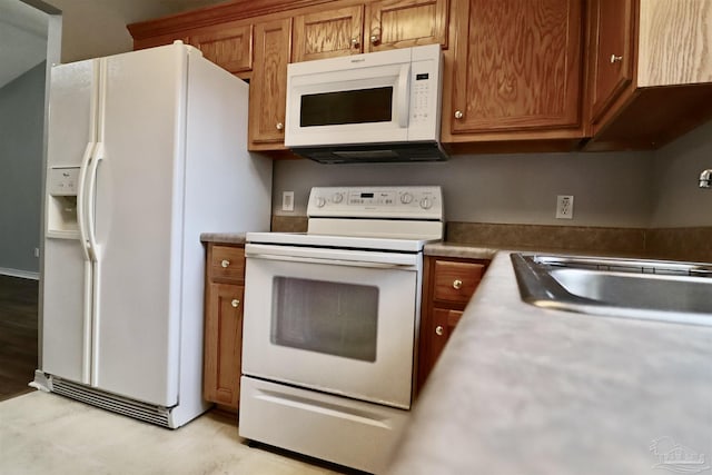 kitchen with a sink, white appliances, and brown cabinets