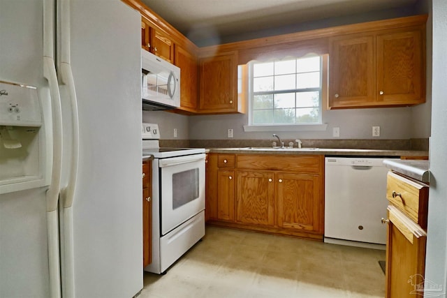 kitchen featuring brown cabinetry, white appliances, and a sink