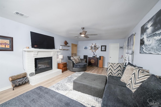 living room with visible vents, baseboards, a fireplace, wood finished floors, and a ceiling fan