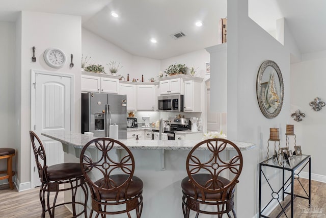 kitchen with light stone counters, white cabinets, appliances with stainless steel finishes, and light hardwood / wood-style floors