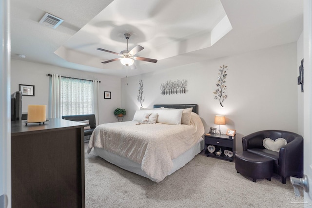 carpeted bedroom featuring a tray ceiling and ceiling fan