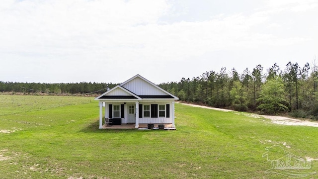 view of front of home with a front yard, covered porch, and a view of trees