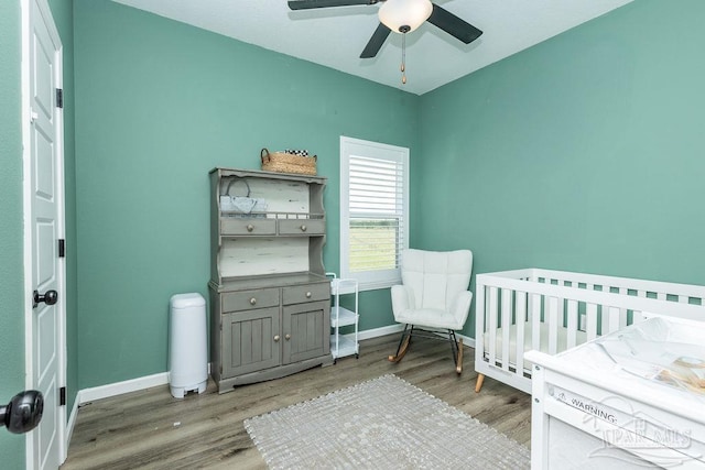 bedroom with baseboards, a ceiling fan, wood finished floors, and a crib