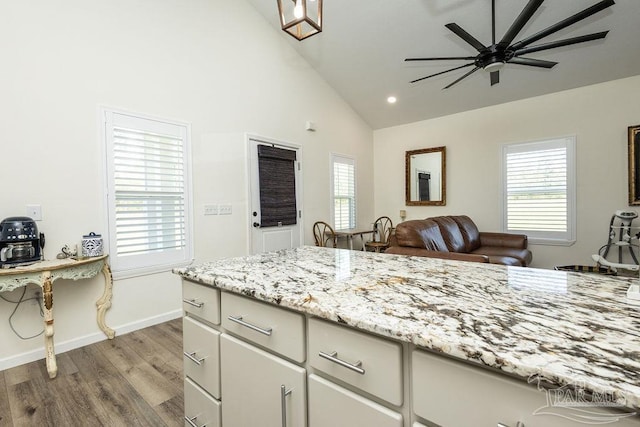 kitchen with open floor plan, baseboards, ceiling fan, light stone countertops, and wood finished floors