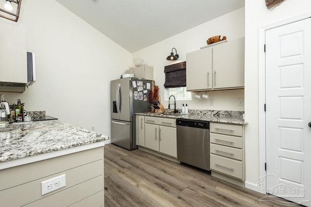 kitchen featuring stainless steel appliances, lofted ceiling, a sink, light wood-style floors, and light stone counters